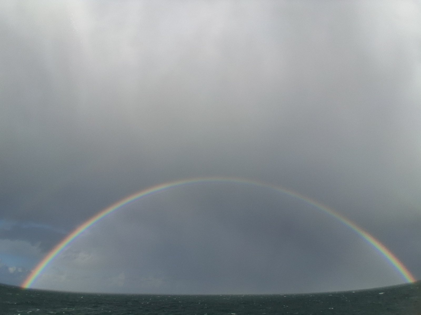 A rainbow over a grey sea, under a passing squall