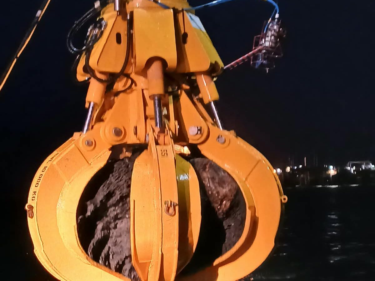 A hydraulic grab lifting rock at night